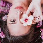 Elegant photoshoot featuring a woman holding a pink flower amidst petals.