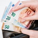 Close-up of a hand holding euro banknotes of different denominations, taken from a black wallet.