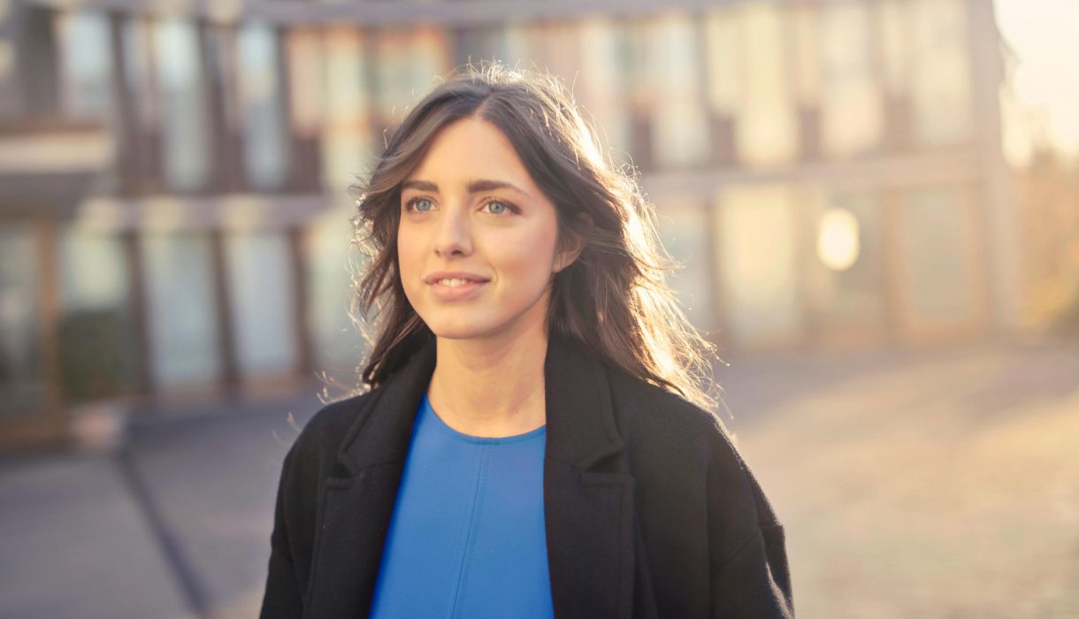 Portrait of a confident woman walking outdoors in an urban setting with a smile.